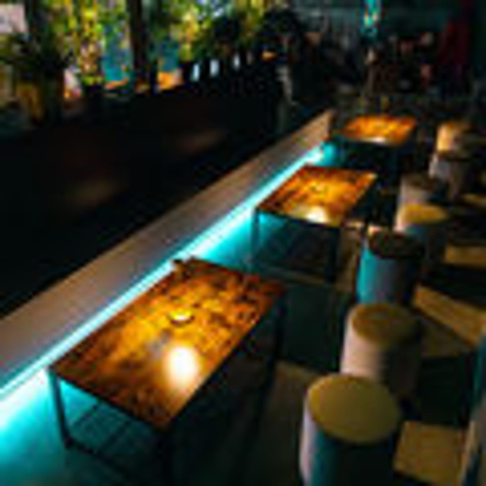 Rooftop bar at night with illuminated tables and stools, creating a vibrant ambiance.