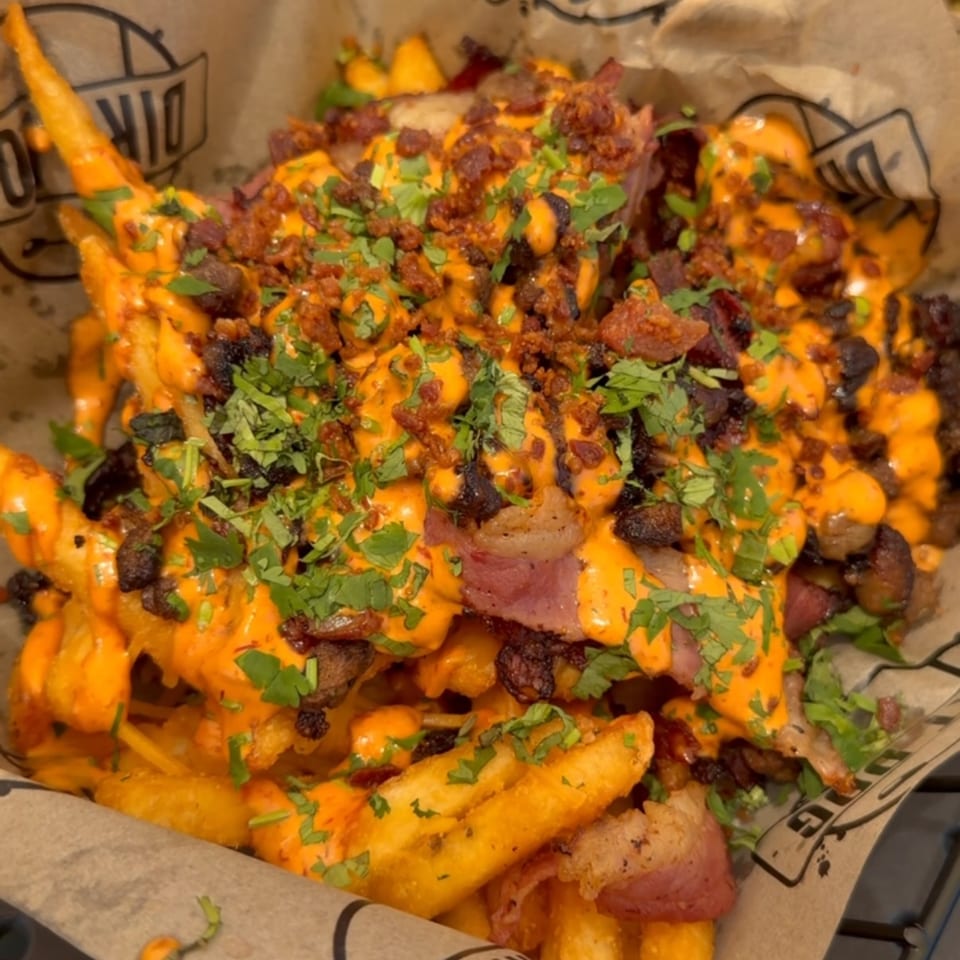 Loaded fries with cheese sauce, bacon, and parsley in a branded paper-lined basket.