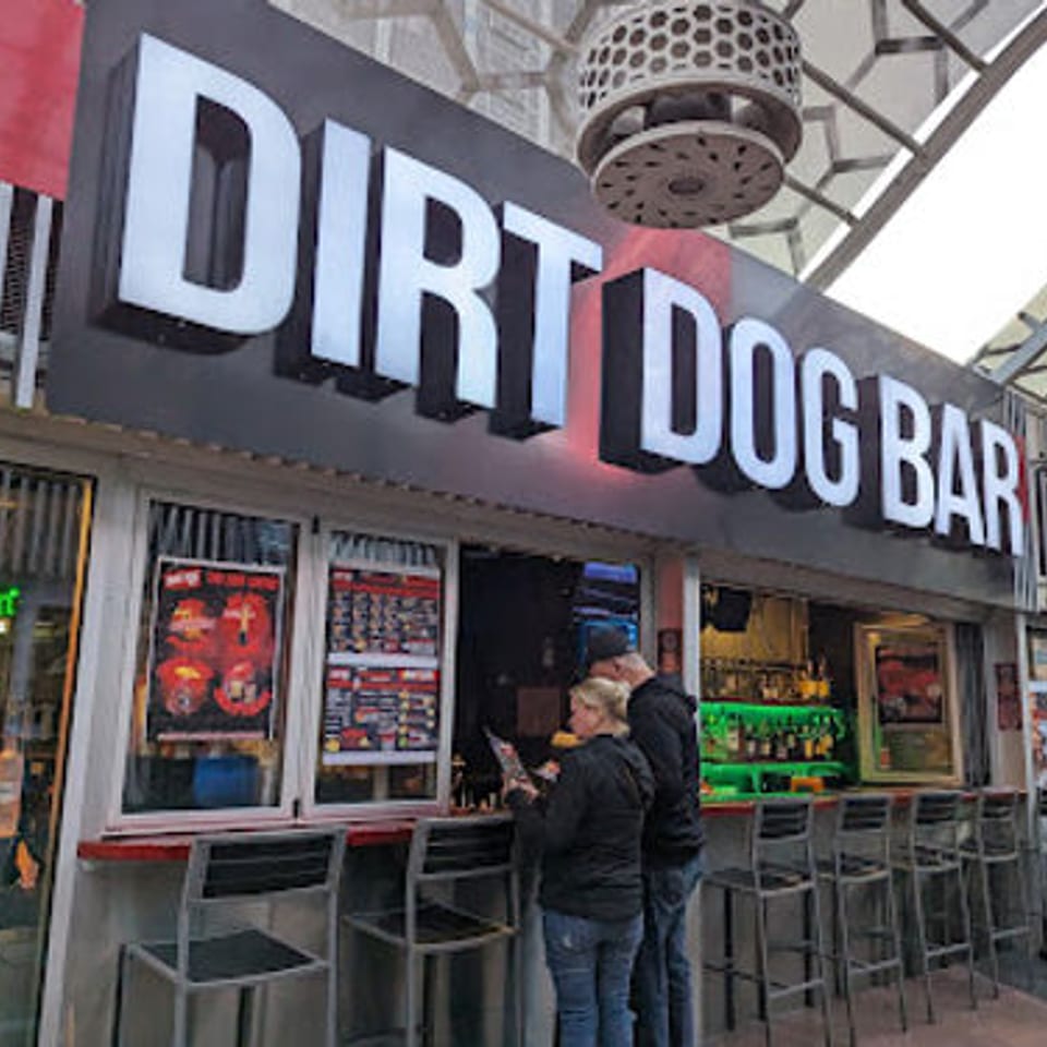Exterior view of Dirt Dog Bar with two patrons standing at the counter and a Heineken sign.