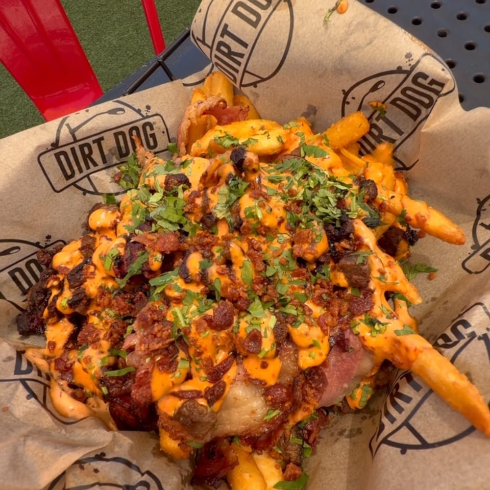 Dirt Dog's loaded fries with cheese sauce, bacon, and cilantro, served on a table outdoors.